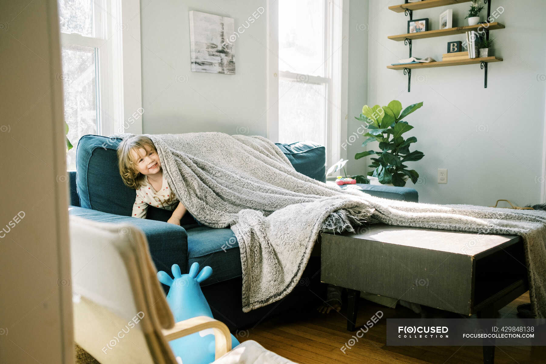 Little girl hiding under a blanket in the living room — silly