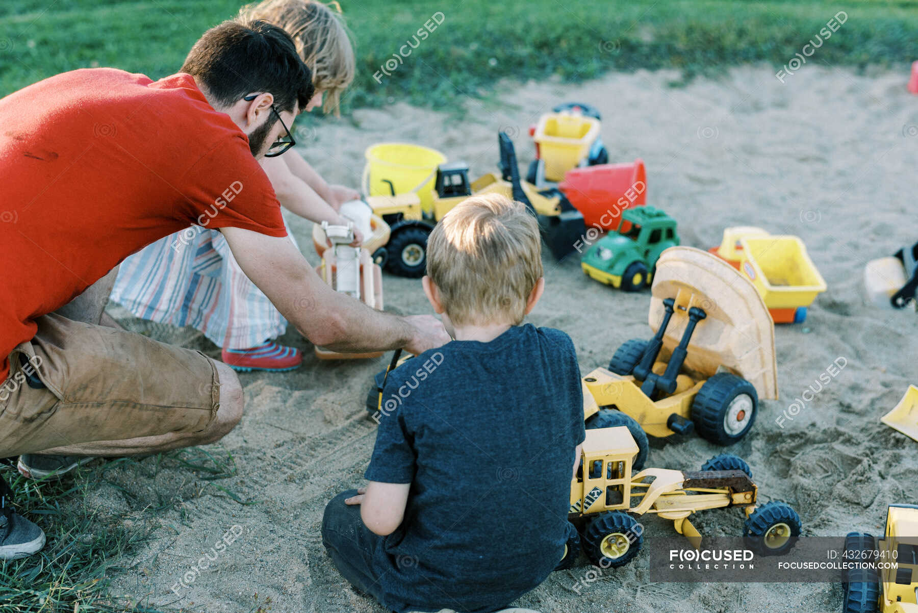 A father and his children playing in a sandbox with trucks together