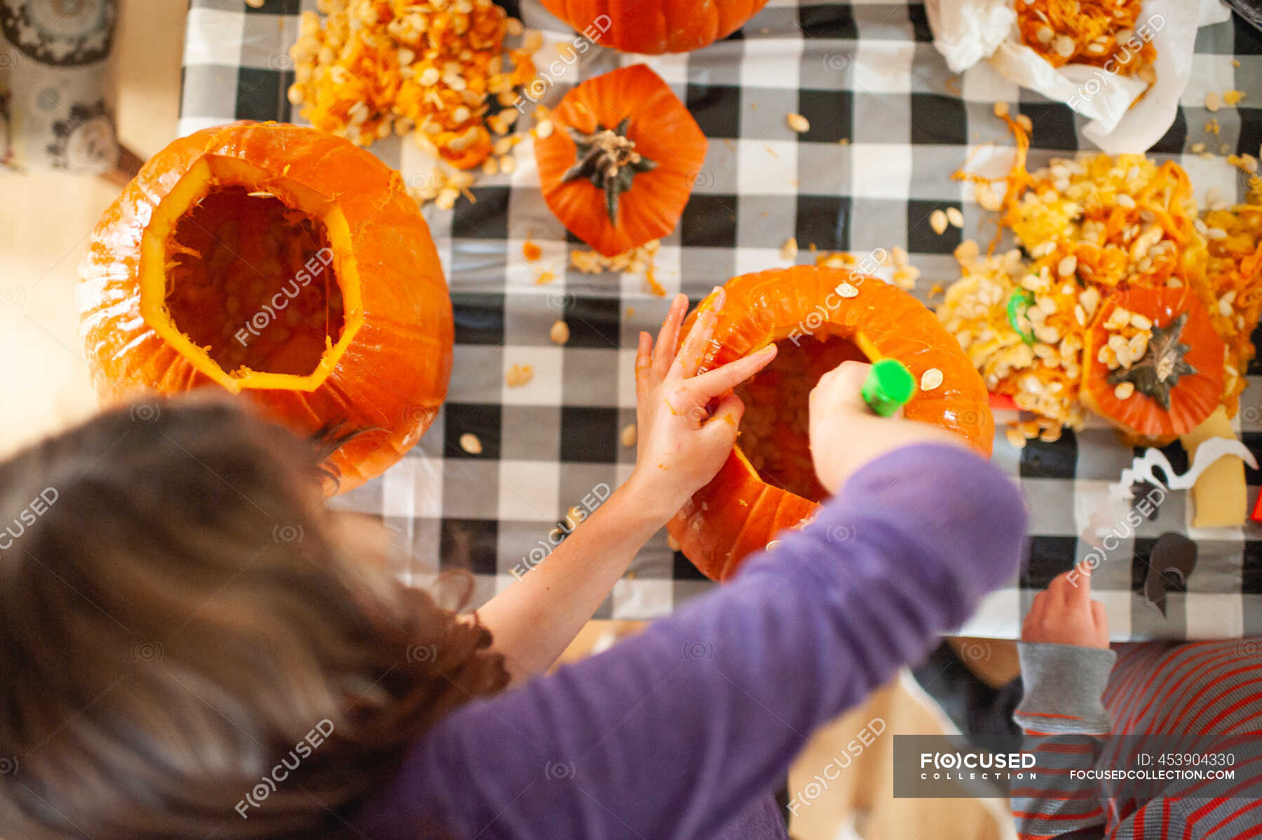 Above head view of kids scooping out pumpkin seeds at table — boy, eve ...