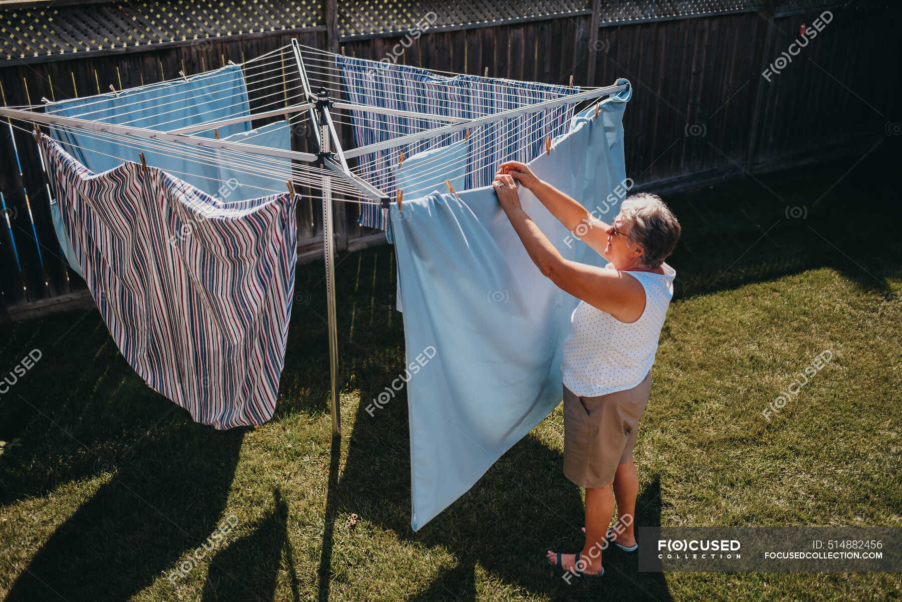 Senior woman hanging laundry on an outdoor clothesline. — age, hair