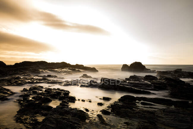 Lunga esposizione, mare, luce serale con nuvole fangose e rocce robuste — Foto stock