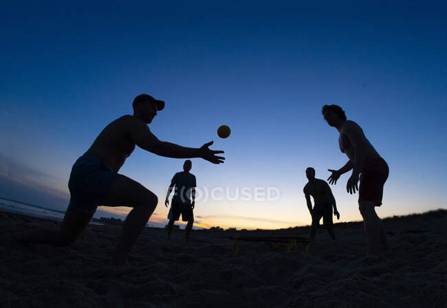 Чотири чоловіки друзі грають м'яч на пляжі в сутінках — стокове фото