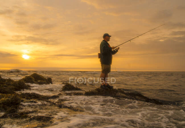 Maine coastal fisherman waits for a striped bass to bite as sun rises. — Stock Photo