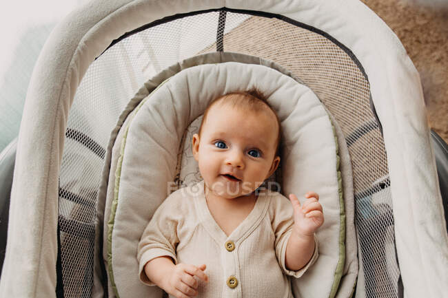 Bebé joven acostado en el moisés y mirando a la cámara y sonriendo - foto de stock