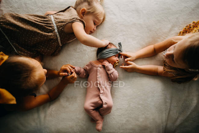 Сестры обнимаются на кровати с новорожденным ребенком — стоковое фото