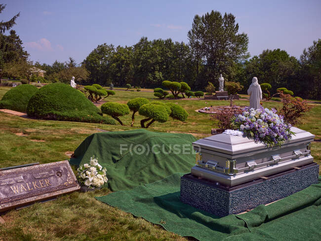 Un ataúd con flores se sienta al lado de una tumba lista para ser enterrada. - foto de stock