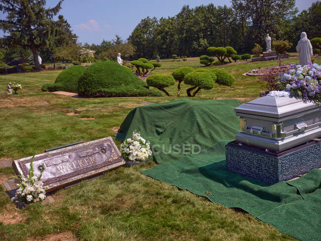 A casket with flowers sits beside a gravesite ready for burial. — Stock Photo