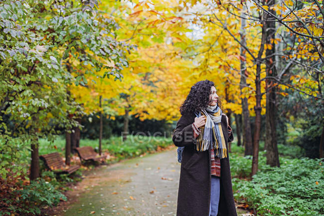 Mujer con abrigo y bufanda caminando en un parque de otoño - foto de stock