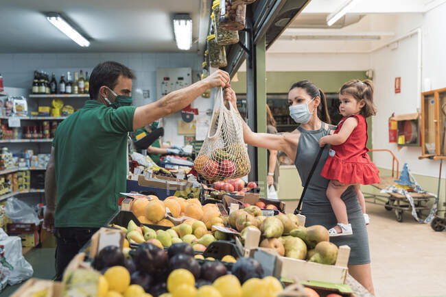 Giovane donna con una maschera shopping al negozio di frutta con sua figlia — Foto stock