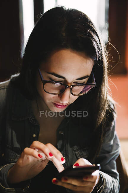 Mulher com óculos usando um telefone celular dentro de um bar — Fotografia de Stock