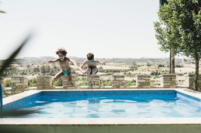 Boy and girl in swimsuit jumping into an outdoor pool in summer — Stock Photo