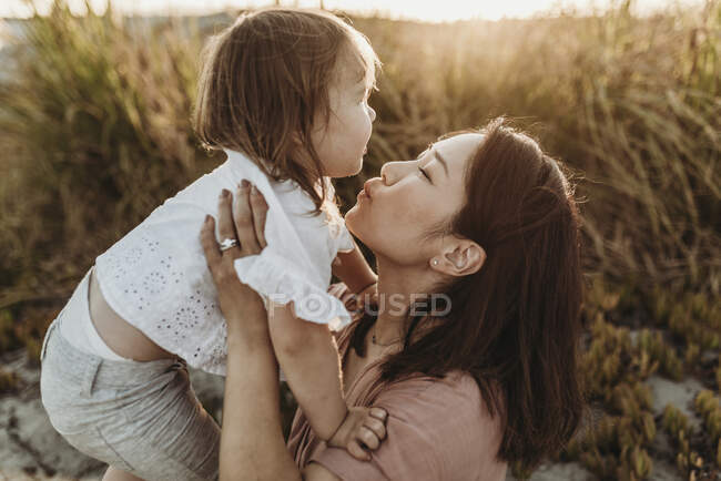 Mãe brincando com 2 anos de idade menina na praia durante o pôr do sol — Fotografia de Stock