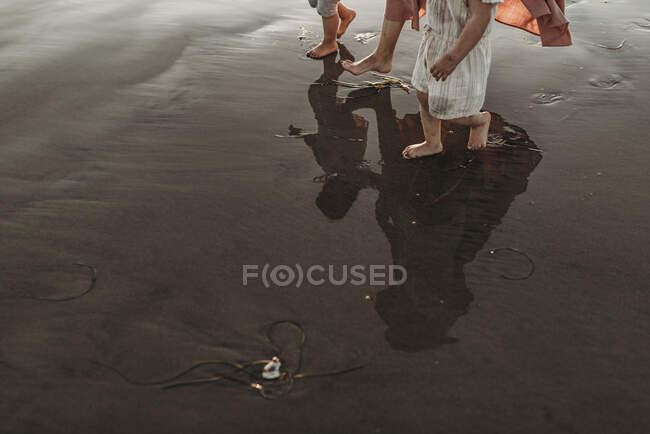 Отражение в океанской воде матери, гуляющей с двумя дочерьми на пляже — стоковое фото
