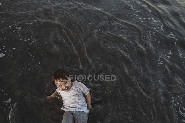 Высокоугольный вид на счастливую девочку, играющую в океане — стоковое фото