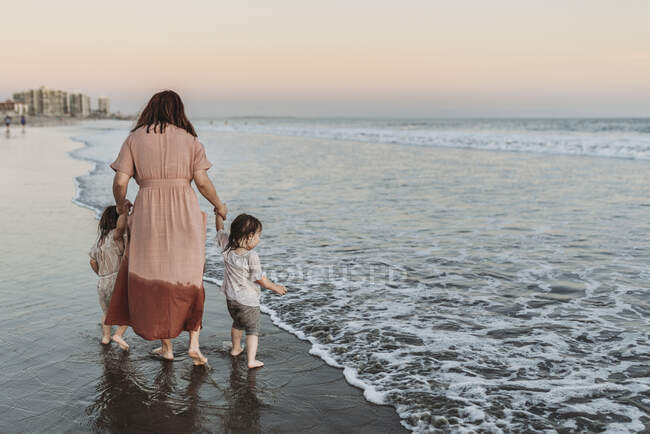 Mère marche avec 2 ans fille à la plage pendant le coucher du soleil — Photo de stock