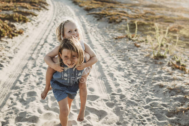 Младшие сестры играют на песке на пляже во время заката — стоковое фото