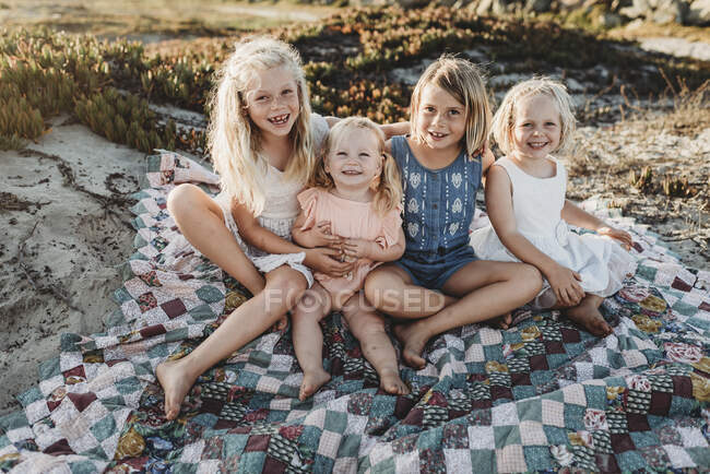 Quatre sœurs assises sur une couverture à la plage souriant au coucher du soleil — Photo de stock