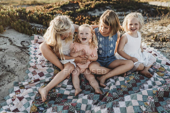 Четыре сестры сидят на одеяле на пляже и смеются на закате — стоковое фото