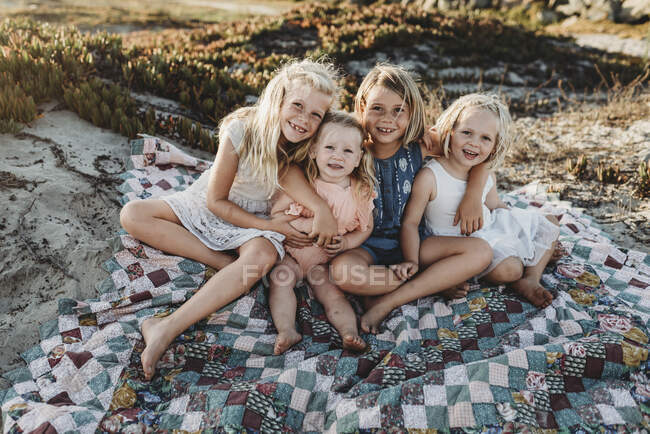 Четыре сестры сидят на одеяле на пляже улыбаясь на закате — стоковое фото