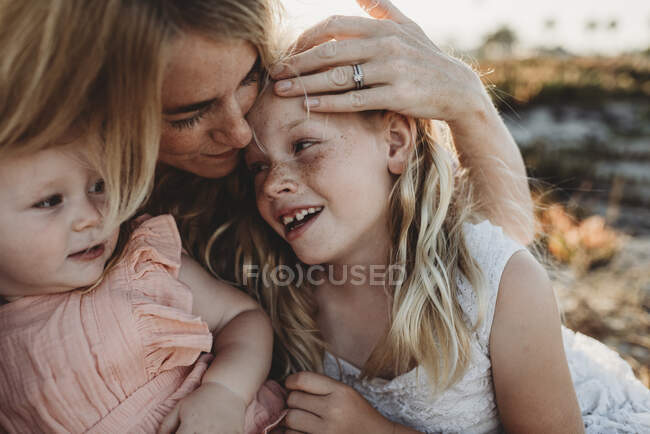 Портрет матери, обнимающейся с маленькими дочерьми на пляже заката — стоковое фото