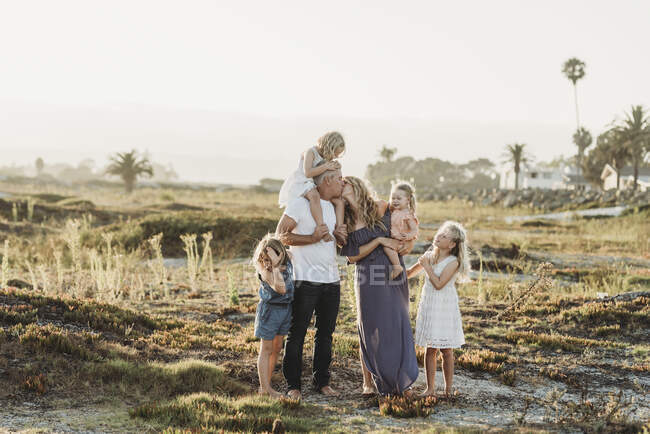 Lifestyle-Porträt einer Familie mit jungen Mädchen, die sich beim Sonnenuntergang am Strand küssen — Stockfoto