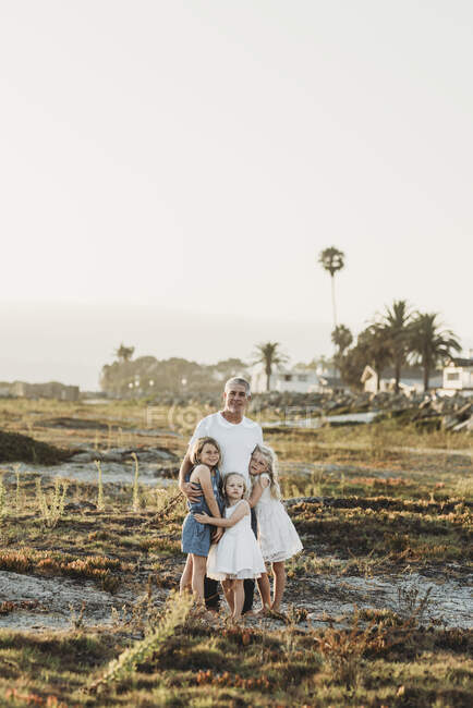 Традиционный портрет отца с юными сестрами, улыбающимися на пляже — стоковое фото