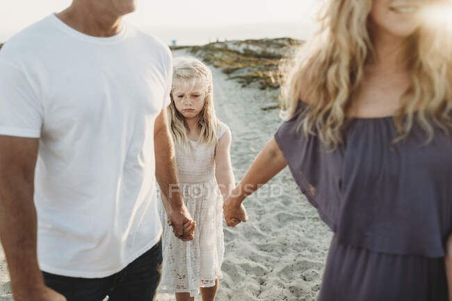 Chica seria haciendo cara triste caminando con los padres en la playa - foto de stock