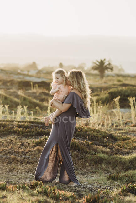 Madre baciare figlia bambino in spiaggia durante il tramonto — Foto stock