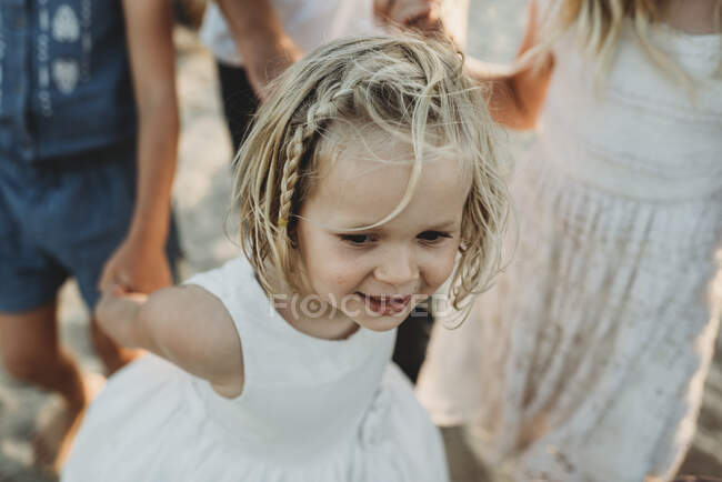 Молода дівчина посміхається і ходить, тримаючи руки сестер — стокове фото