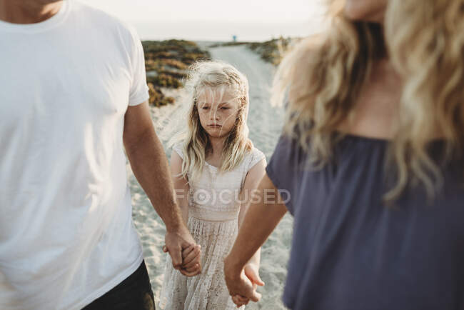 Серйозна дівчина робить сумне обличчя, ходячи з батьками на пляжі — стокове фото