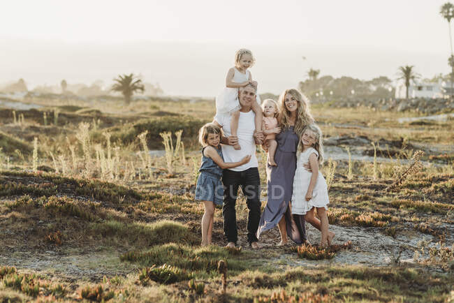 Портрет сім'ї, що стоїть на піску на пляжі під час заходу сонця посміхається — стокове фото