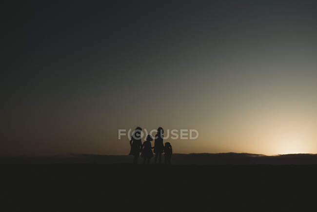 Silhouette de quatre jeunes sœurs à la plage au coucher du soleil — Photo de stock