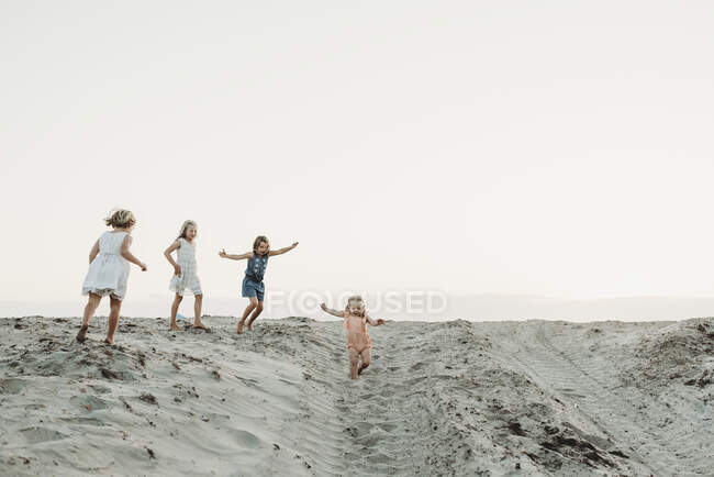 Чотири молодих сестри грають і бігають піском на заході сонця на пляжі — стокове фото