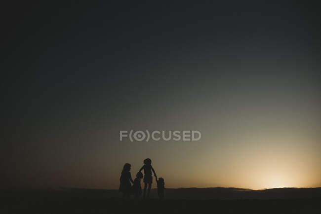 Silhouette di quattro giovani sorelle in spiaggia durante il tramonto — Foto stock