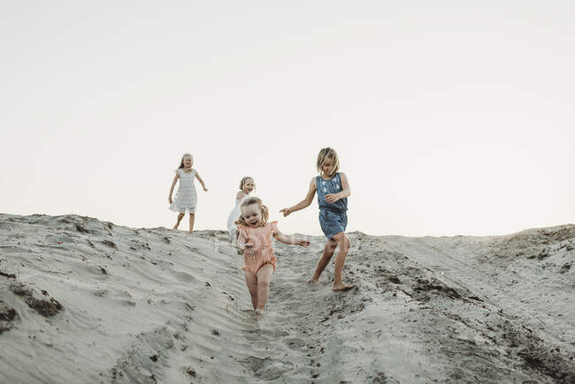 Чотири молодих сестри біжать піском на березі заходу сонця — стокове фото