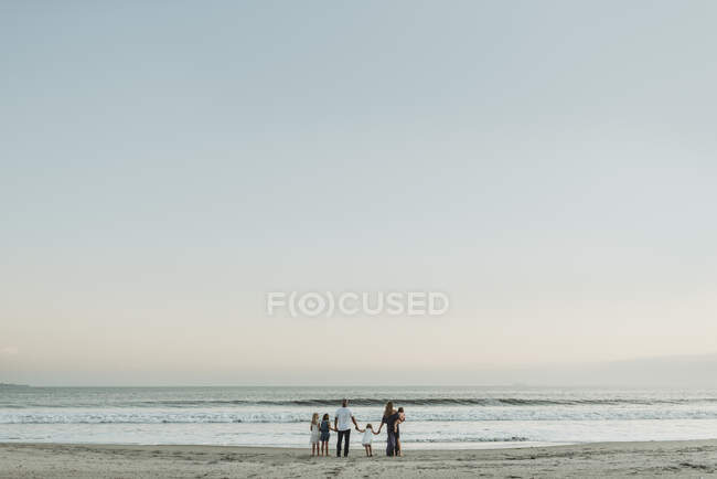 Vista del paisaje de la joven familia de pie en el océano al atardecer - foto de stock