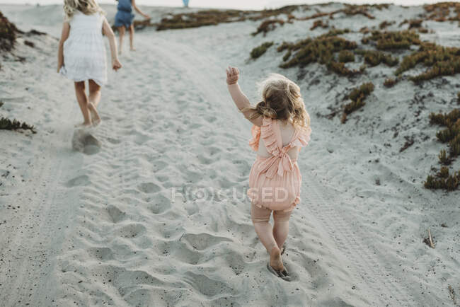 Menina jovem criança perseguindo irmãs mais velhas na praia durante o pôr do sol — Fotografia de Stock