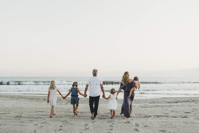 Atrás da vista da jovem família caminhando em direção ao oceano ao pôr do sol — Fotografia de Stock
