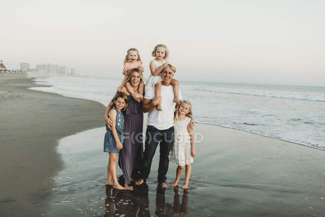Retrato tradicional de familia con cuatro niños sonriendo al sol de la playa - foto de stock