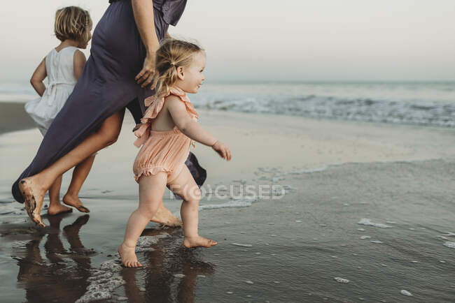Вид сбоку маленькой девочки, бегущей в океан на закате — стоковое фото