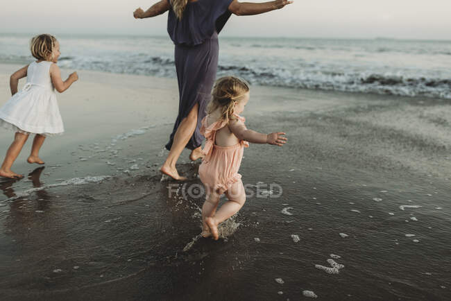Atrás da vista da jovem família caminhando em direção ao oceano ao pôr do sol — Fotografia de Stock