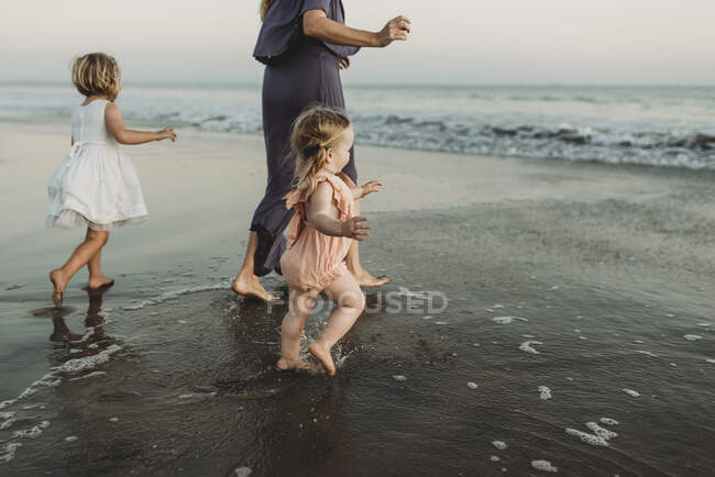 Vue de derrière de la jeune famille marchant vers l'océan au coucher du soleil — Photo de stock