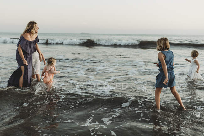 Strong mother with four daughters playing in ocean at sunset — Stock Photo