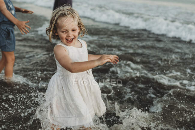 Девочка дошкольного возраста в белом платье играет в океане на закате — стоковое фото