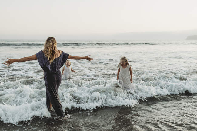 Мама и две молодые девушки брызгают в океан на закате — стоковое фото