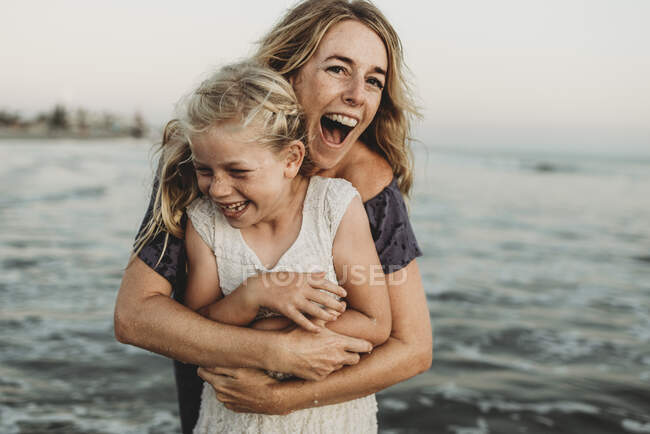 Mother embracing young girl with freckles in ocean laughing — Stock Photo