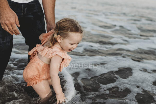 Маленькая девочка плескается в океане с отцом на закате — стоковое фото