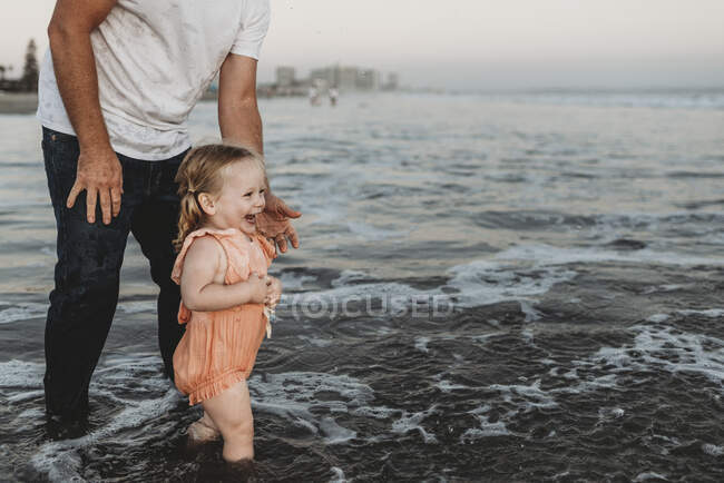 Menina criança espirrando no oceano com o pai ao pôr do sol — Fotografia de Stock
