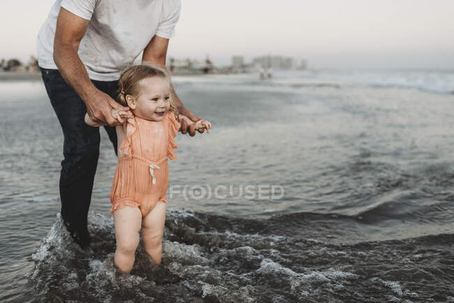 Toddler girl splashing in ocean with father at sunset — Stock Photo