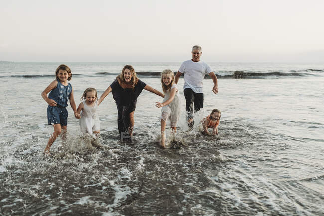 Сім'я з чотирма дівчатами грає і бризкає хвилями на заході сонця — стокове фото